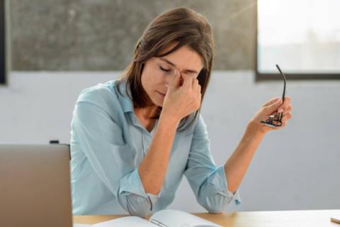 Caucasian woman at desk with paperwork and glasses off rubbing her face