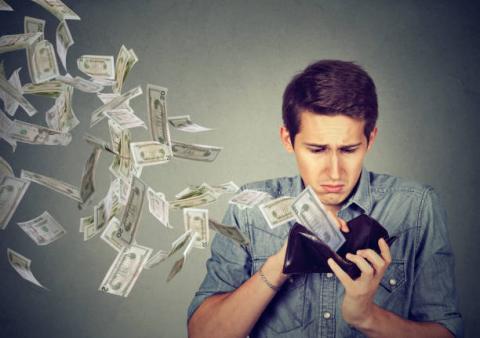 Man looking in wallet while money notes fly out of it