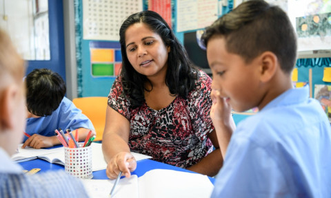 Teacher at table with students pointing at page in book