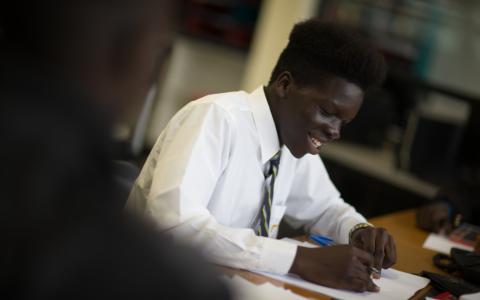 Male student sitting at table and writing on a piece of paper.